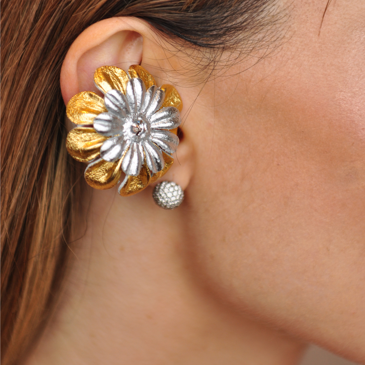 PERIPHERII PRIAMBLE Gita Bluetooth earbuds, close-up of gold outer petals and silver inner petals with a crystal center.