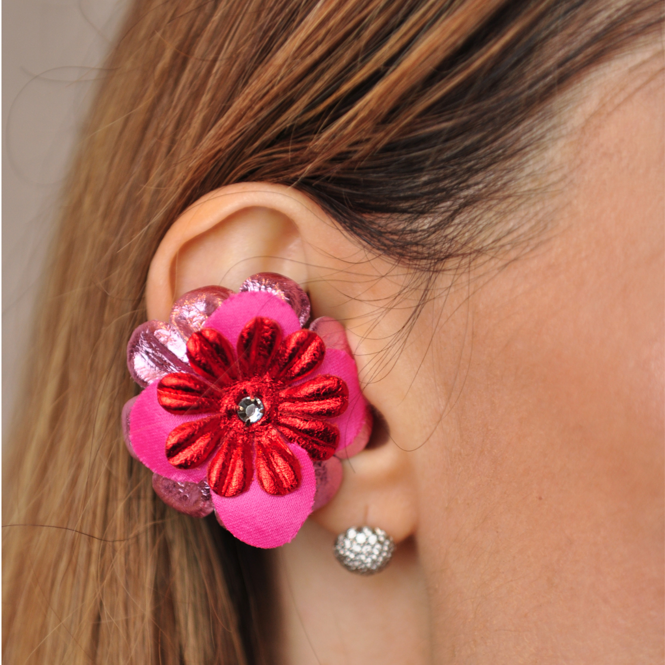 Priamble Audio Earrings In Fuchsia and red with a crystal center in closeup of a woman's ear