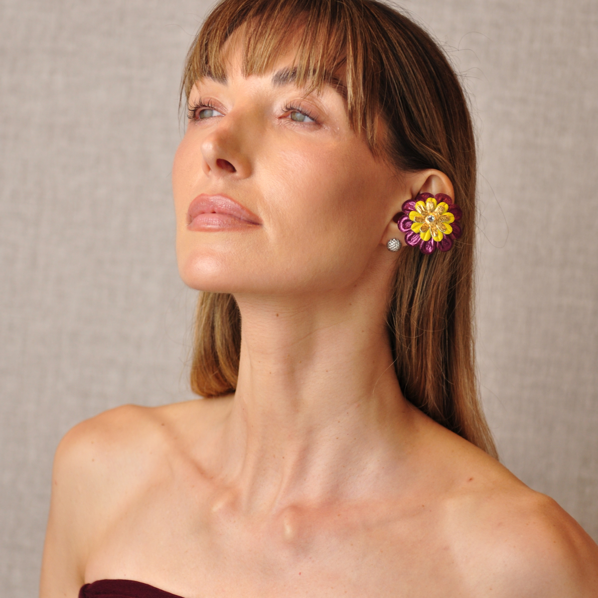 Young woman in an angled portrait wearing PERIPHERII PRIAMBLE Gita burgundy-and-yellow floral Bluetooth earbuds.
