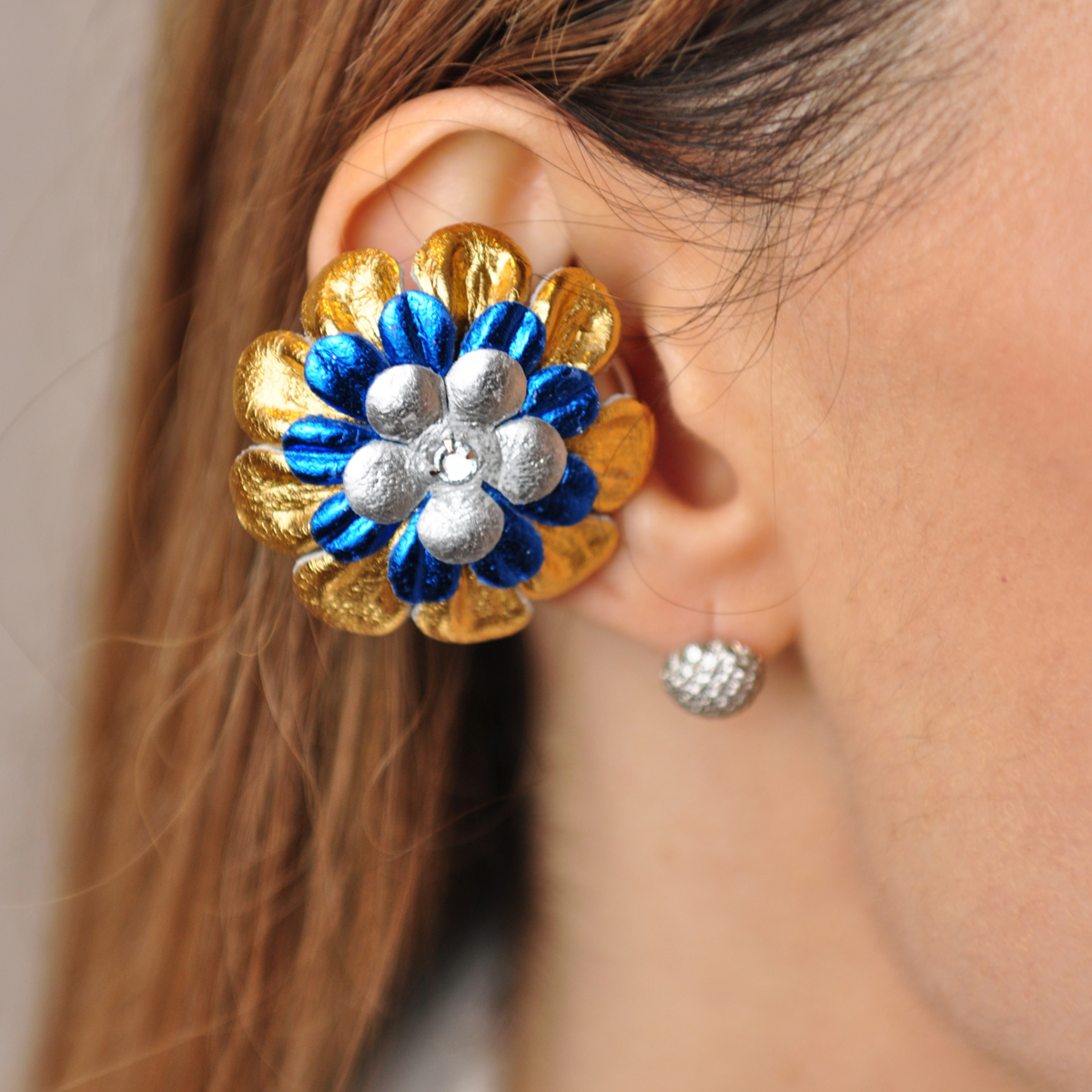 PERIPHERII PRIAMBLE Gita Bluetooth earbuds, close-up of gold, cobalt-blue and silver petals with a crystal center.