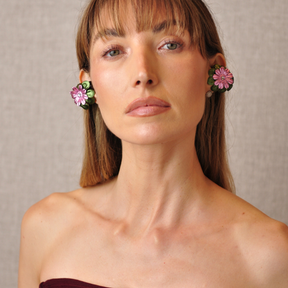 Front view of a young woman wearing PERIPHERII PRIAMBLE Gita Bluetooth earbuds with olive-green and pink floral petals.