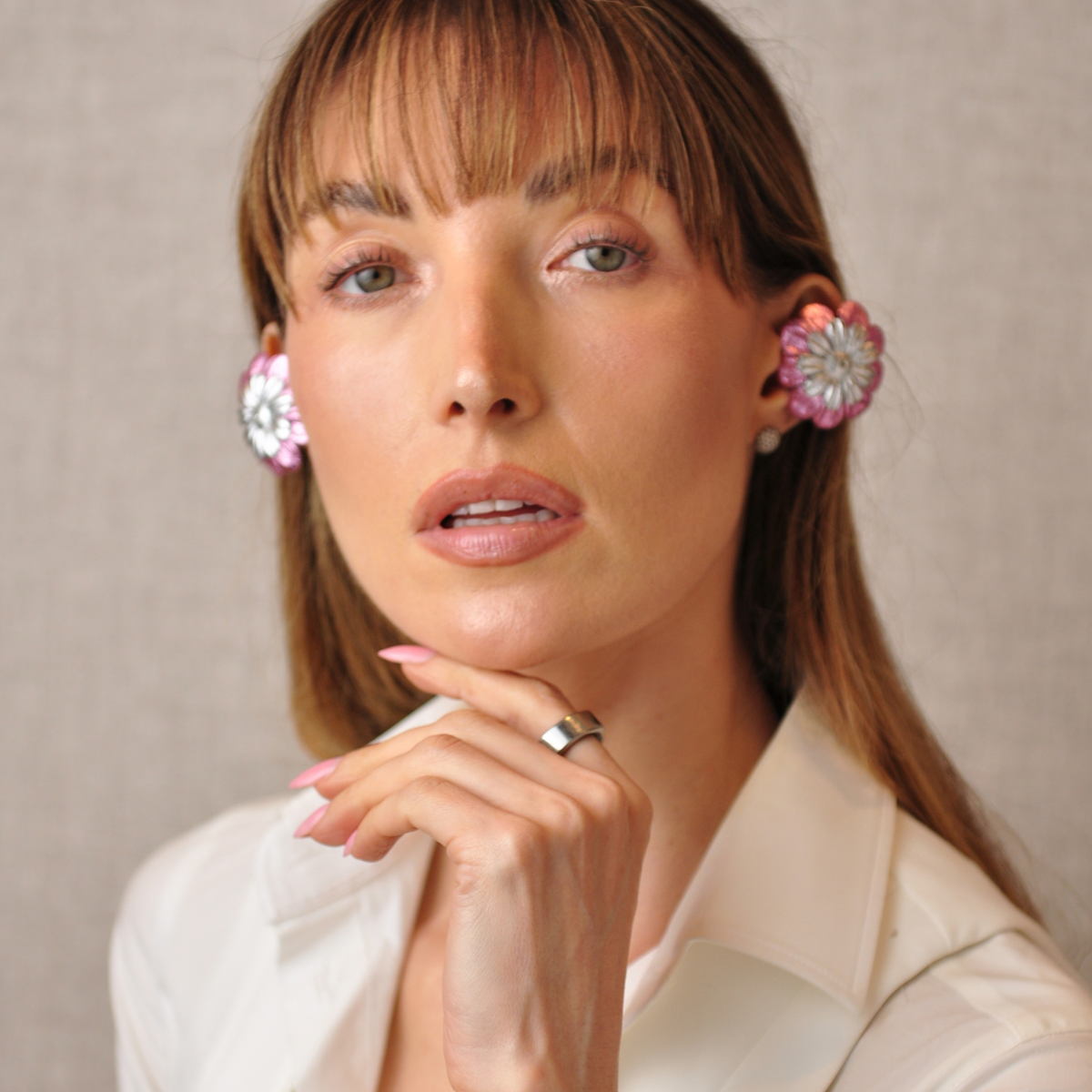 Young woman resting her hand beneath her chin, wearing PERIPHERII PRIAMBLE Gita pink-and-silver Bluetooth earbuds.