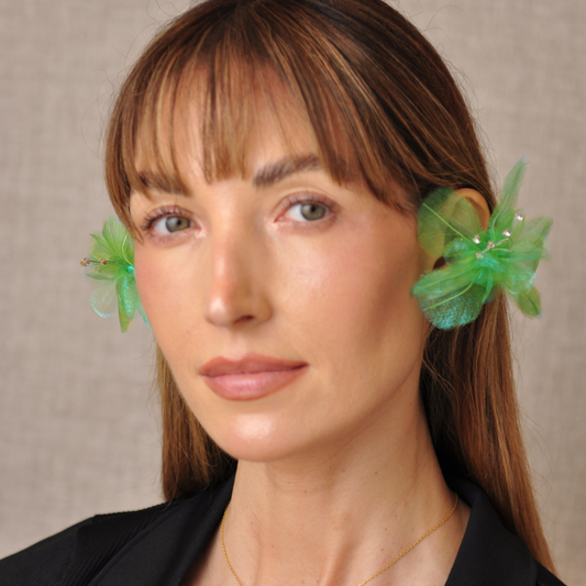 Front view of a model wearing green PRIAMBLE Sonnet audio earrings with sheer orchid petals and crystal accents.
