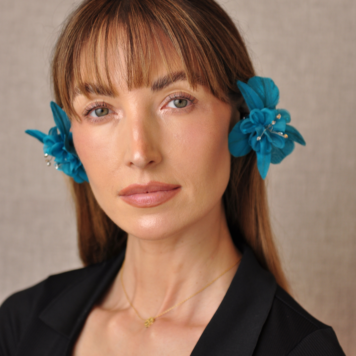 Front view of a model wearing teal PRIAMBLE Sonnet audio earrings with layered orchid petals and crystal accents.